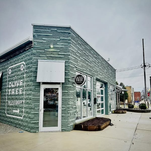 The Olive Tree Marketplace storefront in Casey, Illinois — a green stone building with painted window signage and a planter beside the front door