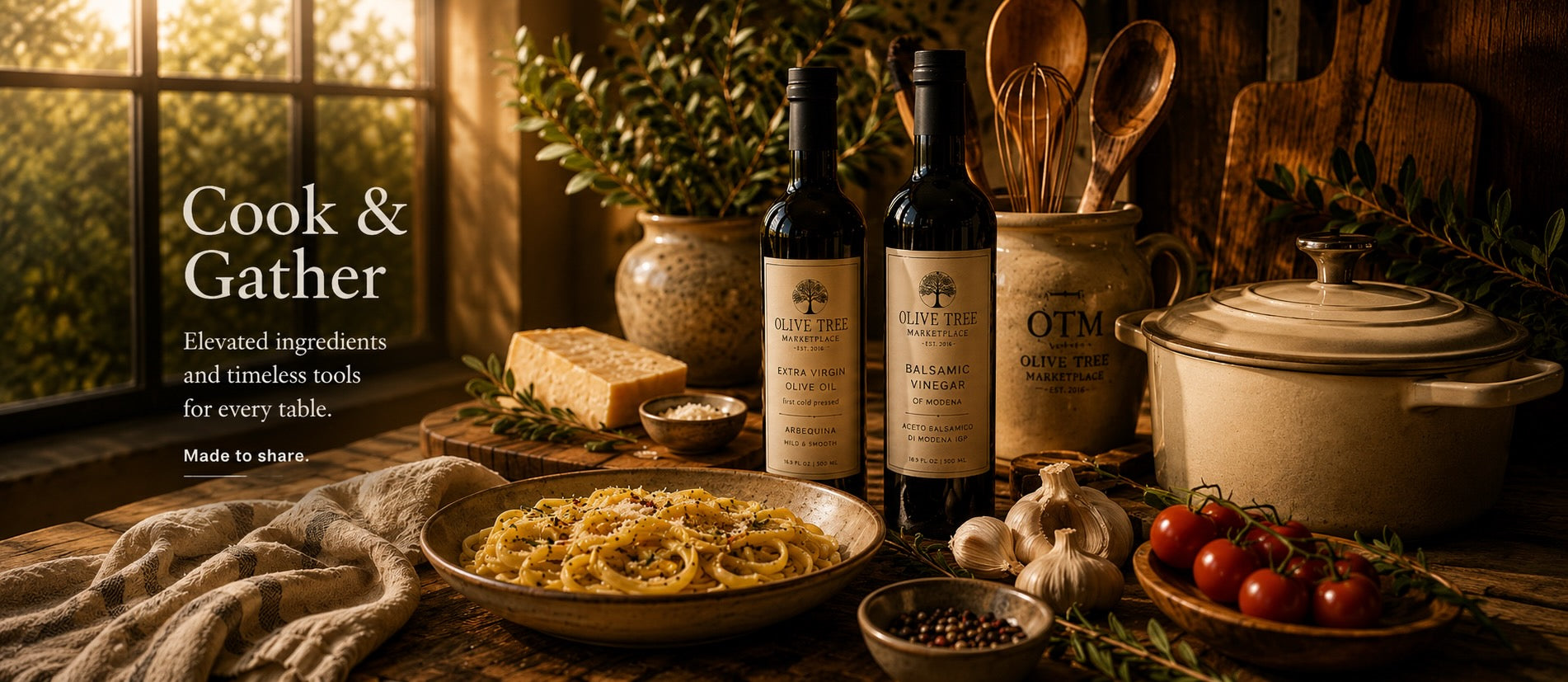 Olive Tree Marketplace kitchen table laid for cooking — olive oil and balsamic vinegar bottles, a ceramic Dutch oven, wooden utensils, a bowl of pasta, garlic and tomatoes
