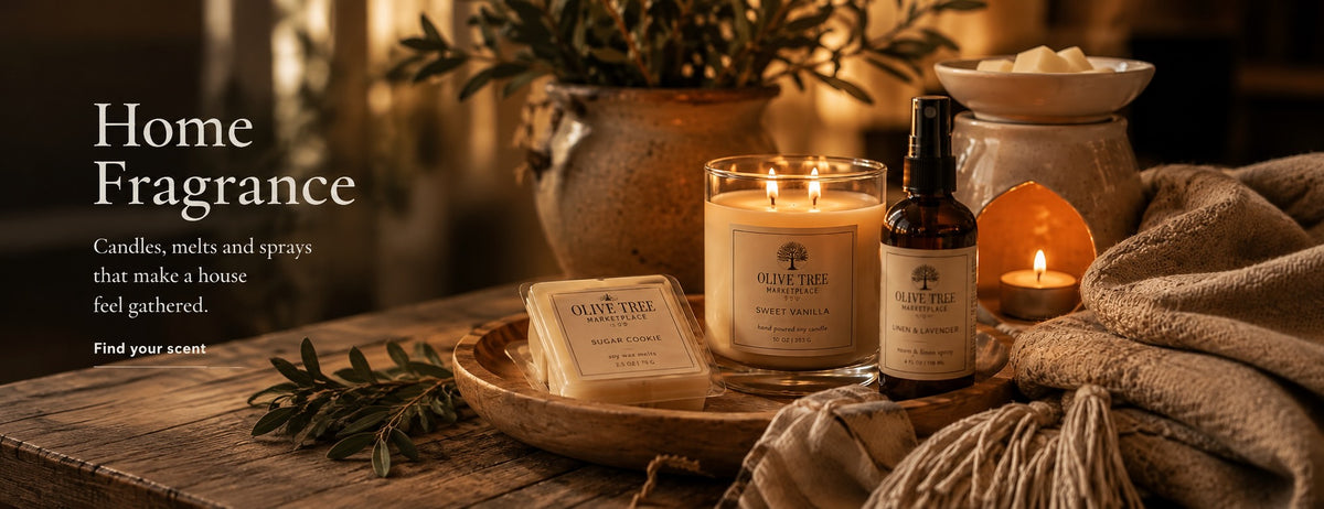 Olive Tree Marketplace home fragrance collection — lit soy candles, a wax melt bar and a room spray on a wooden tray with a chunky knitted throw